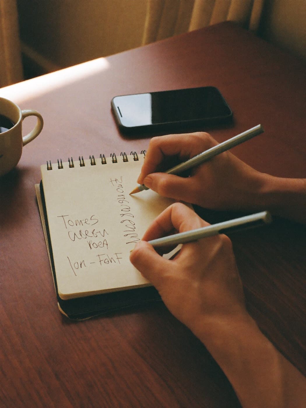 Manos escribiendo en una libreta junto a un café